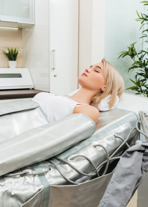 Blonde girl lying with closed eyes during pressotherapy session in clinic